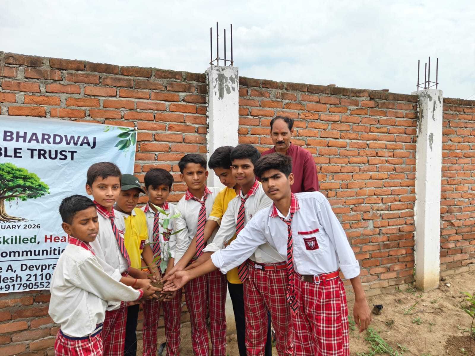 Students and a supervisor planting a sapling beside the trust banner